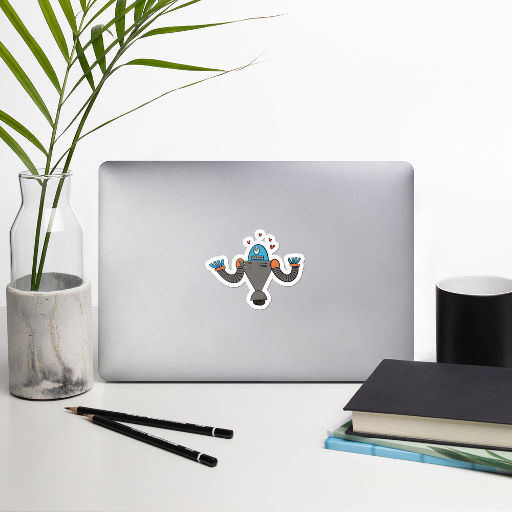 A robot doodle with a "heart eyes" expression has been made into a sticker and is stuck to a laptop.