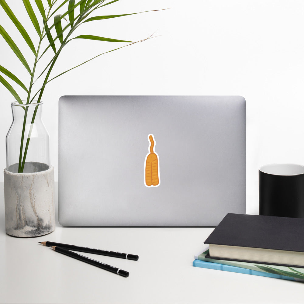 A sticker of an orange cat butt doodle is on a laptop surrounded by office supplies.