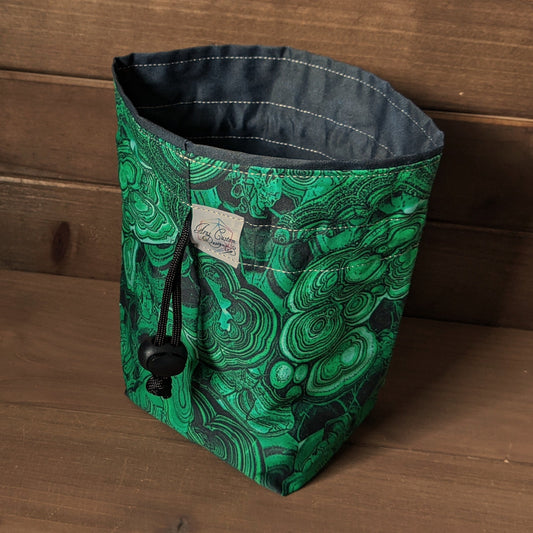 A square bottomed drawstring bag with malachite print fabric sits on a wood surface.