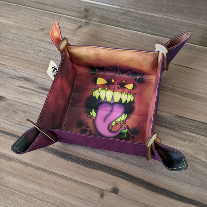 A dice tray with blue/purple/red fabric outside and a mimic face print in the center sits on a wood surface with wood clips in the corners.