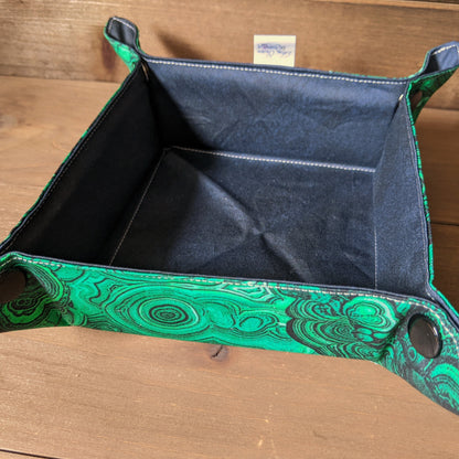 A dice tray with malachite print fabric outside, a dark tonal fabric inside, and black capped snaps sits on a wood surface.