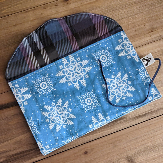 A pen roll with white snowflakes made of skulls on the bright blue pocket and a liner of blue and lavender plaid.