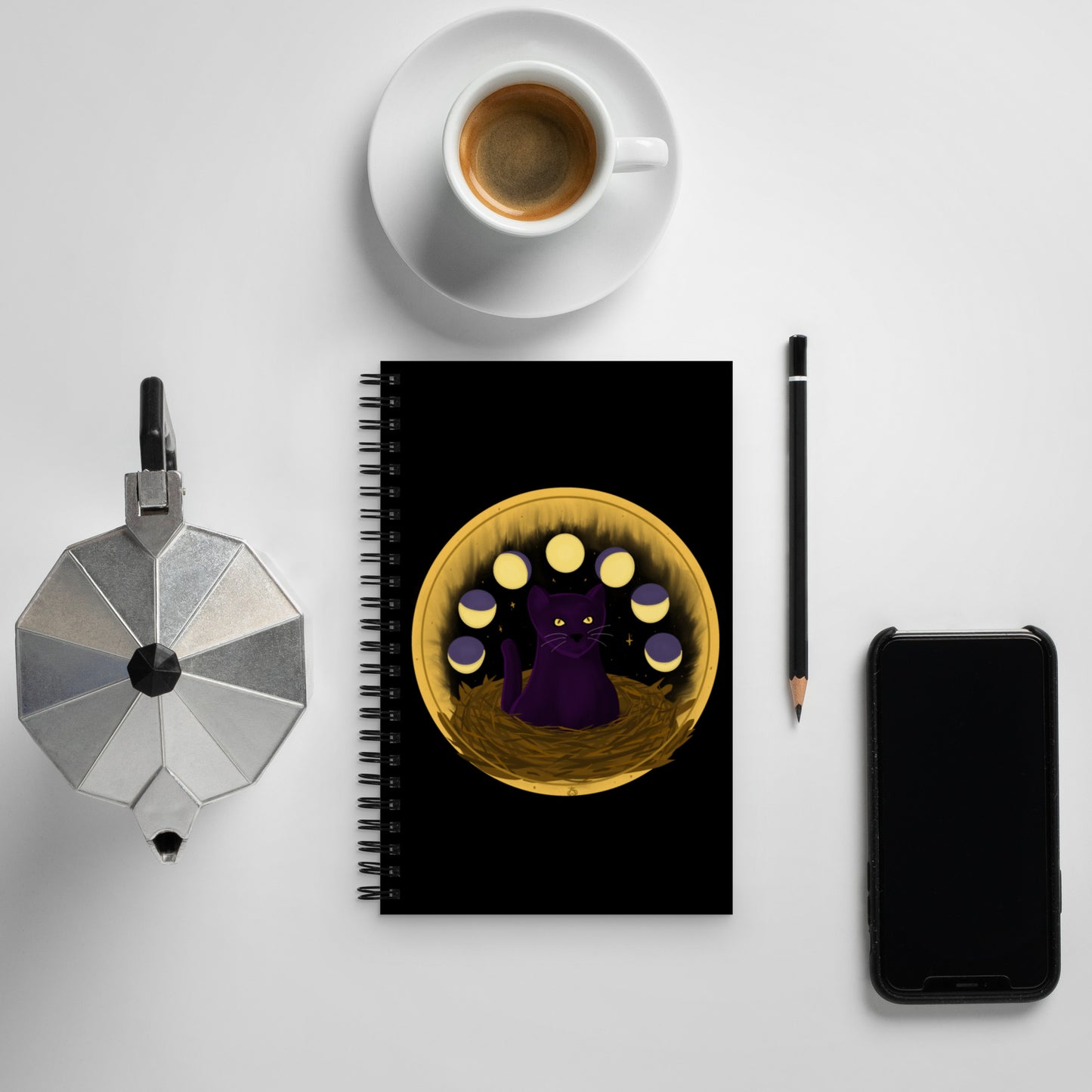 A black notebook with a painting of a dark purple cat with golden eyes sitting in a nest, ringed by the phases of the moon and golden stars behind it.