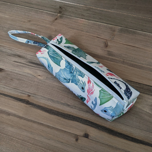 A rectangular bag with a zipper in the middle, a wrist strap, and green and blue watercolor dragons all over it.